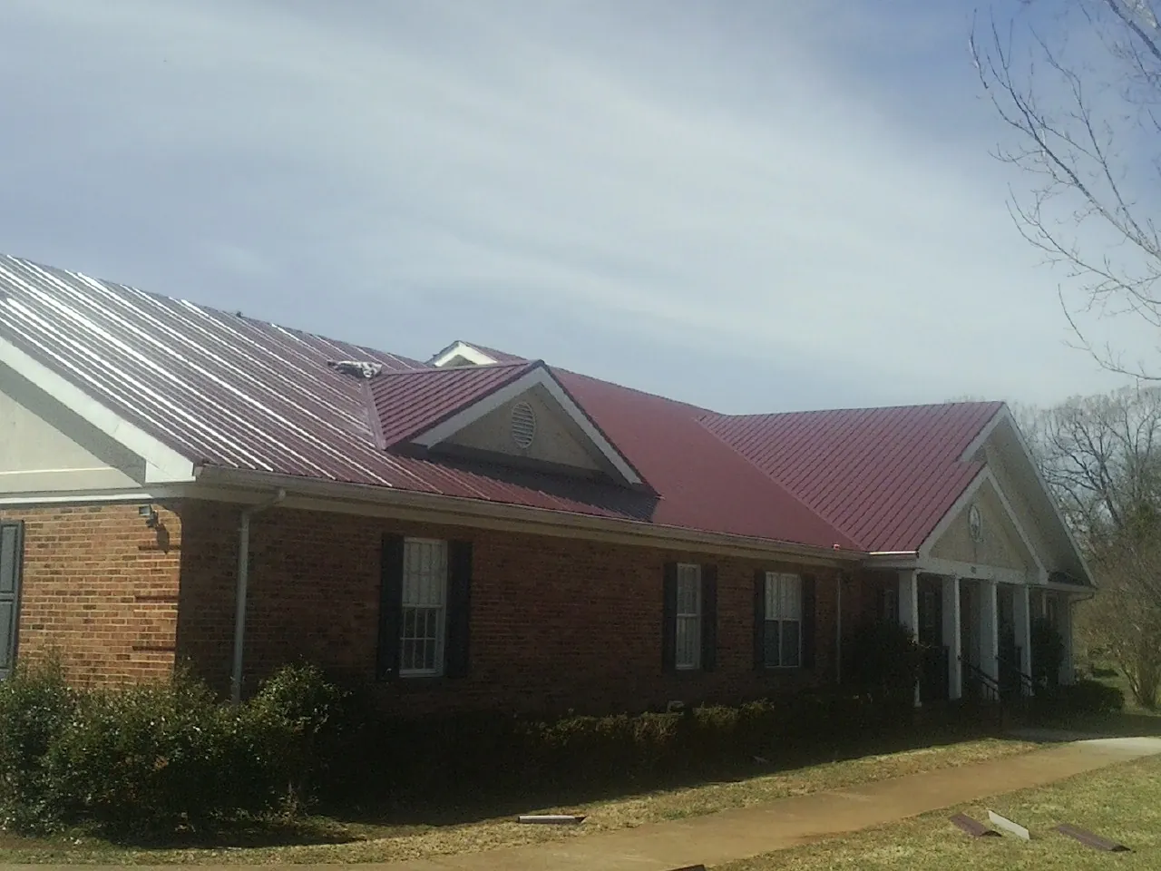 Red metal roof with gabled entries on a long brick building, from a Hail Damage Roof Repair job in Edinburg