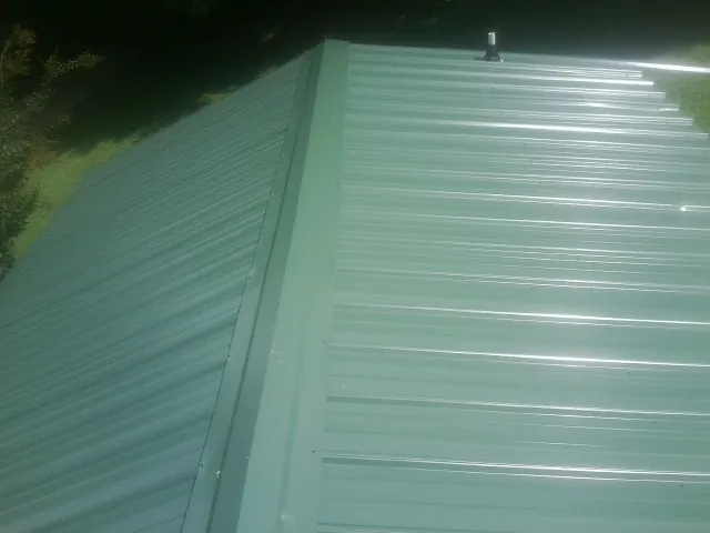 New green metal panels meeting at the ridge of a roof — Flat Roof Repair work by our crew in Edinburg