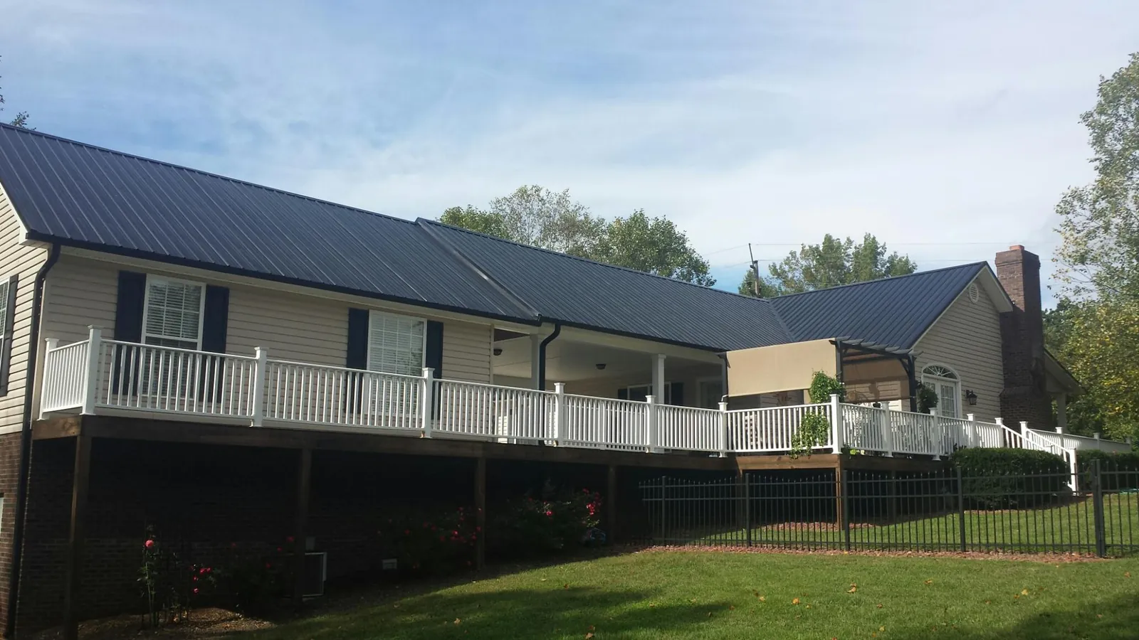Black metal roof above a long white railed deck on a hillside home in Edinburg