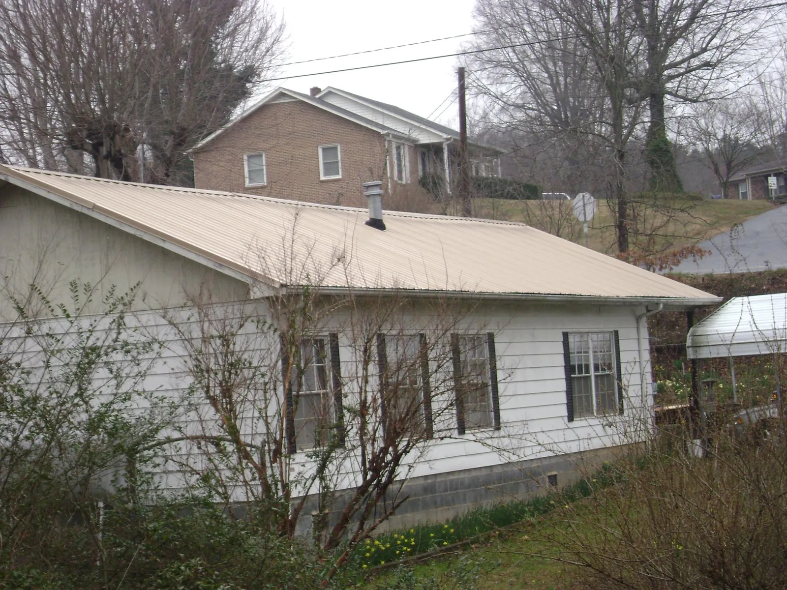 Tan metal roof on a white sided house set into a hillside — Commercial Roofing by Roofing Brothers in Edinburg
